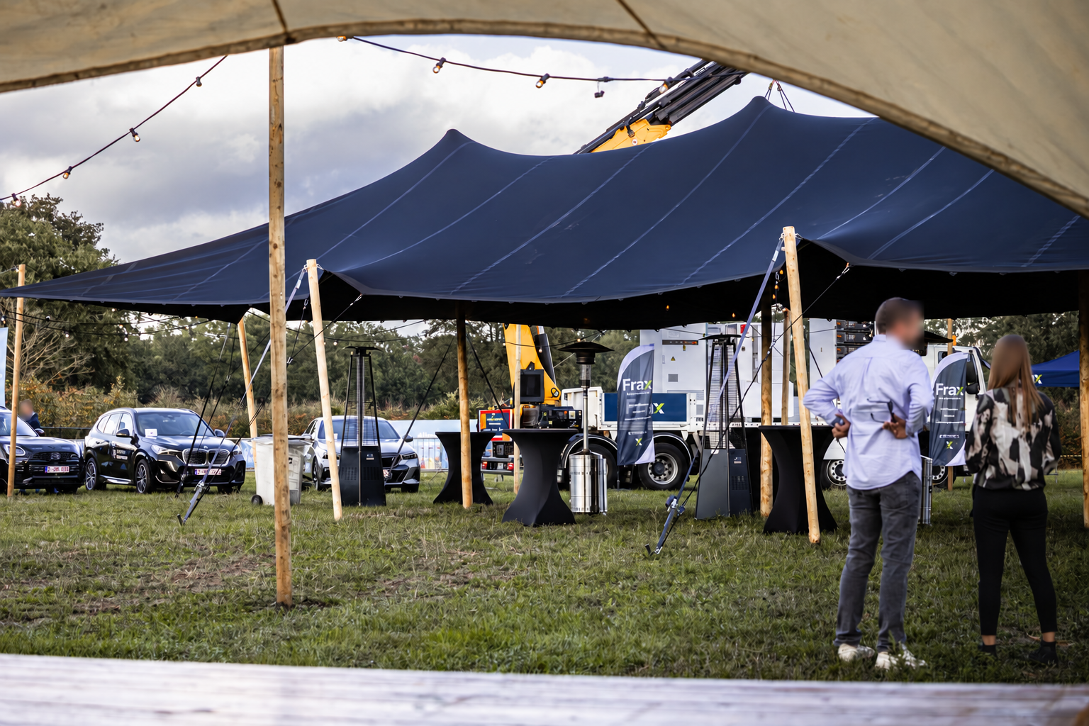 De open stretchtent met houten palen en statafels tijdens een event